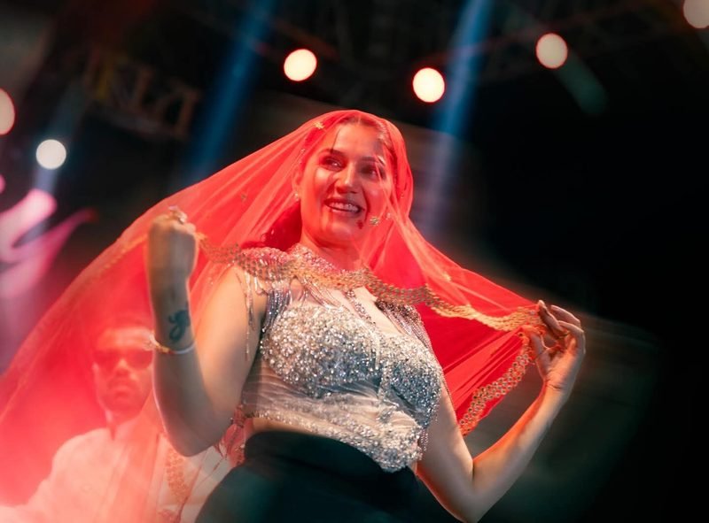 Sapna Choudhary wedding and sangeet performance booking Sapna Choudhary dancing with a red dupatta under red stage lights during a wedding sangeet style performance.