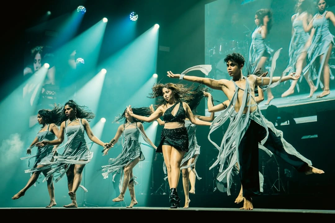 Sunidhi Chauhan performing with dance troupe on teal-lit arena stage — TKC Talent